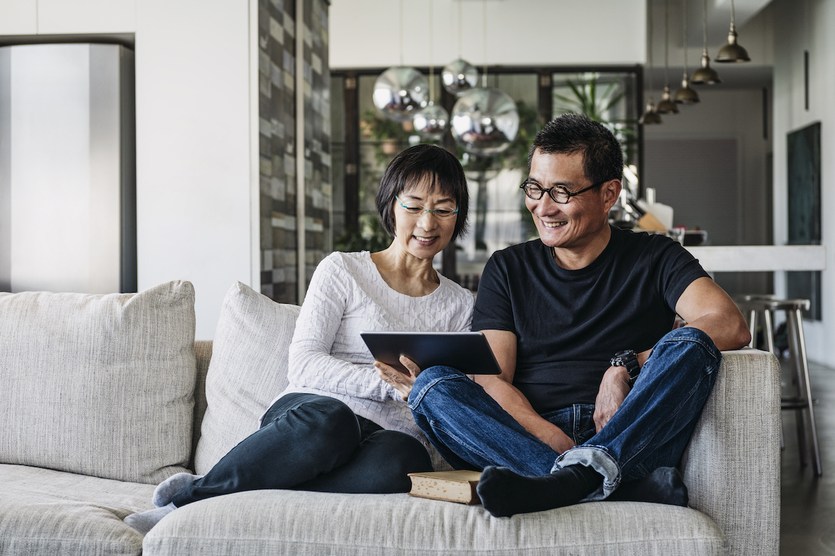 A man and woman sitting on the couch looking at an ipad.